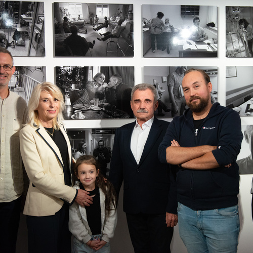 Autorzy wystawy pozują do wspólnego zdjęcia razem z osobą po transplantacji i jego rodziną na tle czarno-białych fotografii.