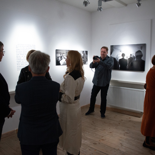 Goście galerii oglądają czarno-białe fotografie i prowadzą rozmowy podczas wernisażu wystawy.