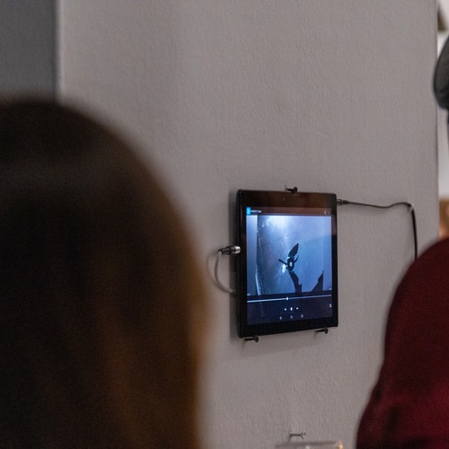 Zwiedzający w słuchawkach oglądają film wyświetlany na tablecie zamontowanym na ścianie galerii.