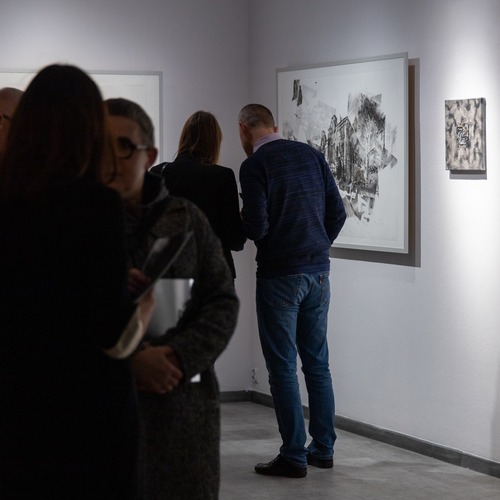 Zwiedzający podczas wernisażu skupieni wokół czarno-białych grafik architektonicznych.