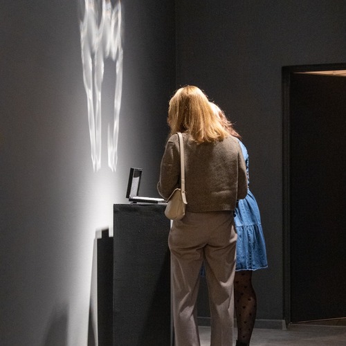 Dwie kobiety oglądają eksponat rzucający na ścianę refleks w kształcie dłoni.