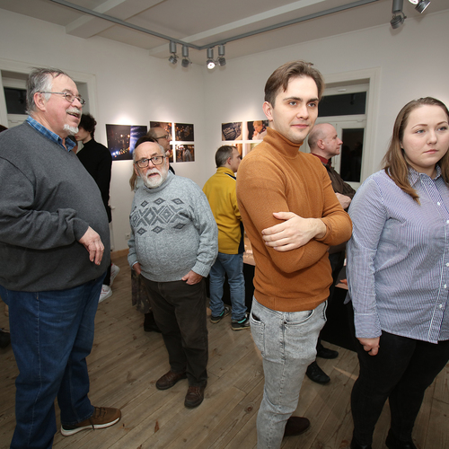 Grupa osób zwiedza wystawę fotograficzną w galerii, oglądając zdjęcia zawieszone na ścianach.